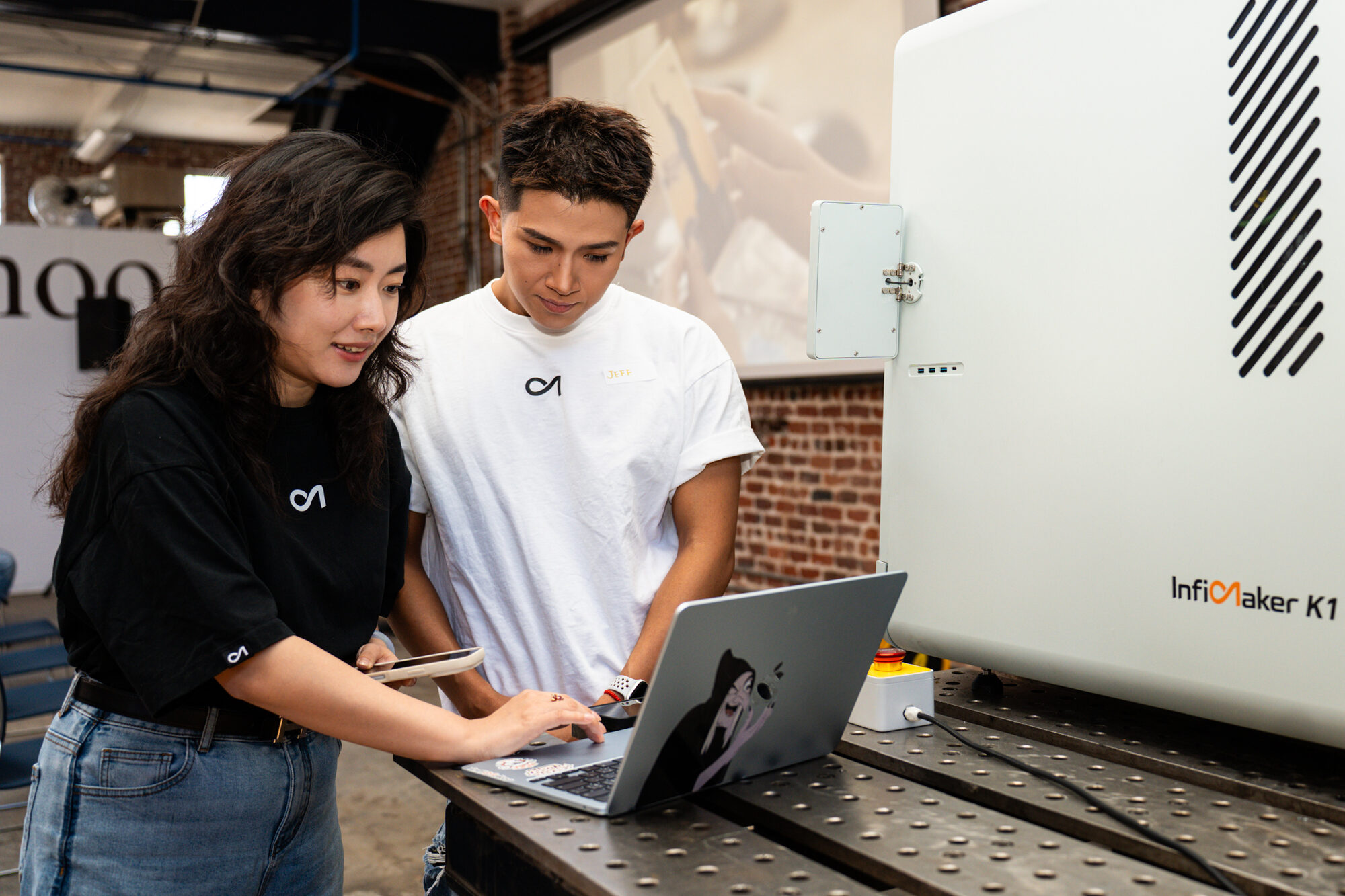 Two people at a laptop beside the InfiMaker K1